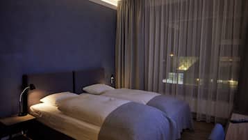 Ein modernes Hotelzimmer mit einem großen Bett, einem Nachttisch, einer Lampe und Blick durch leichte Vorhänge.