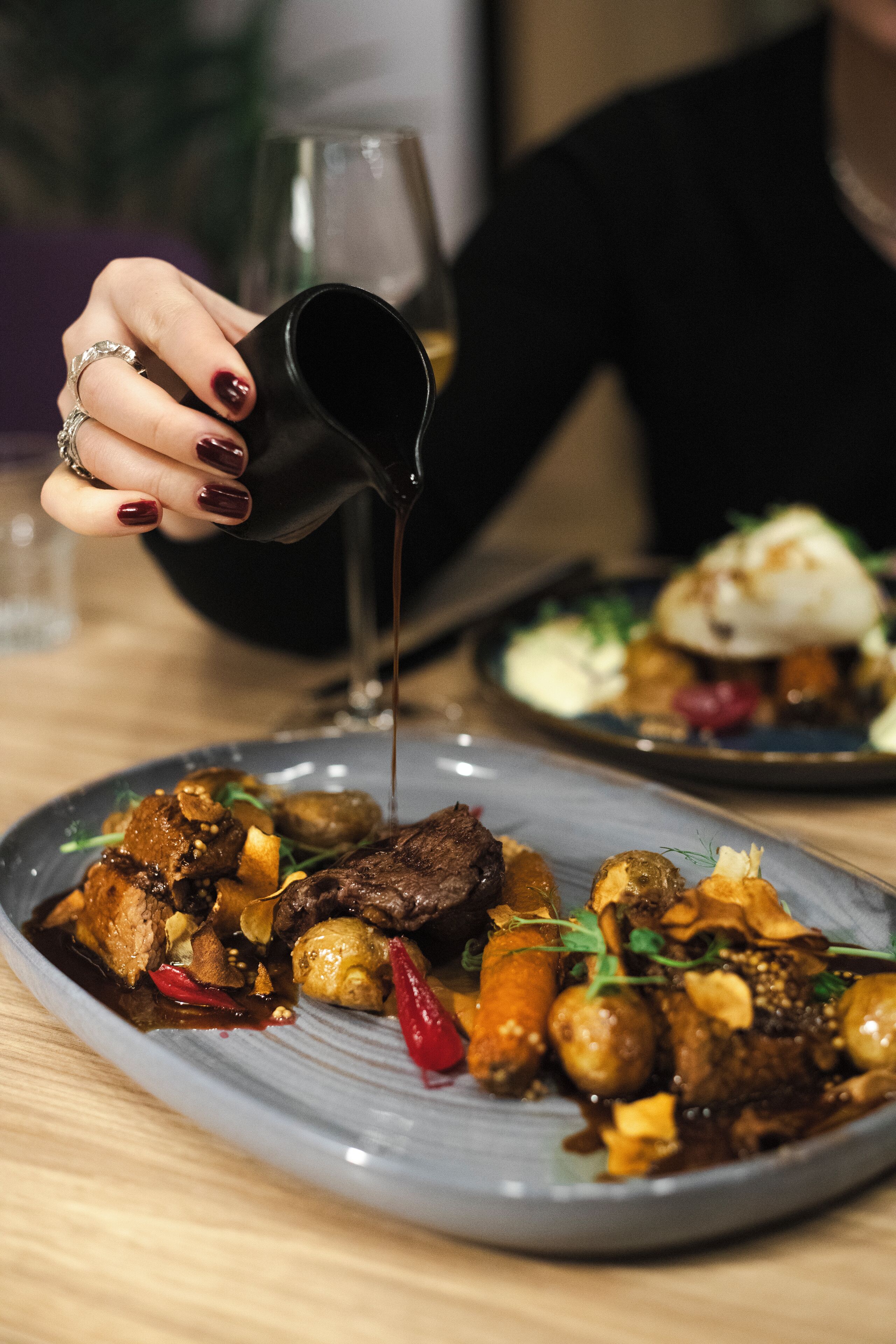 A person pouring a dark liquid onto a plate of food.