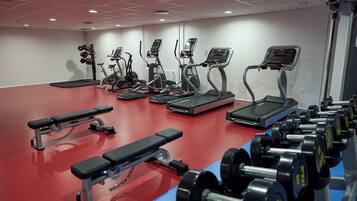 Un gimnasio con cintas de correr, elípticas, una banca y mancuernas.