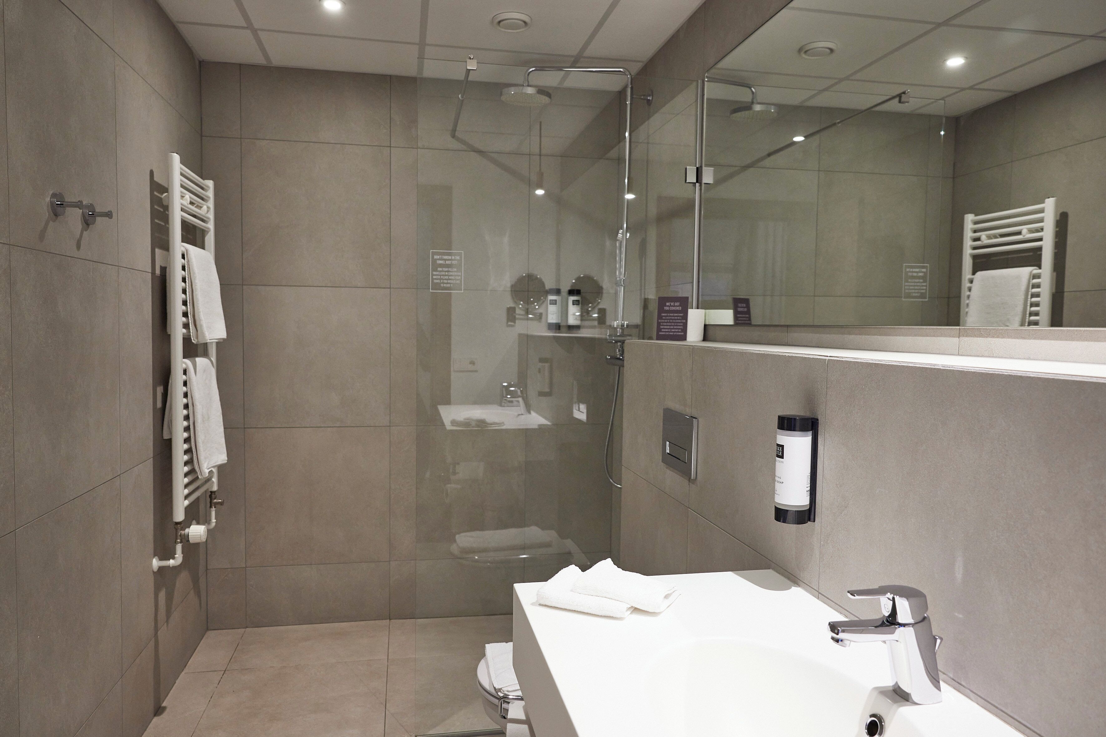 Un baño moderno con ducha de vidrio, lavamanos blanco y un espejo grande.