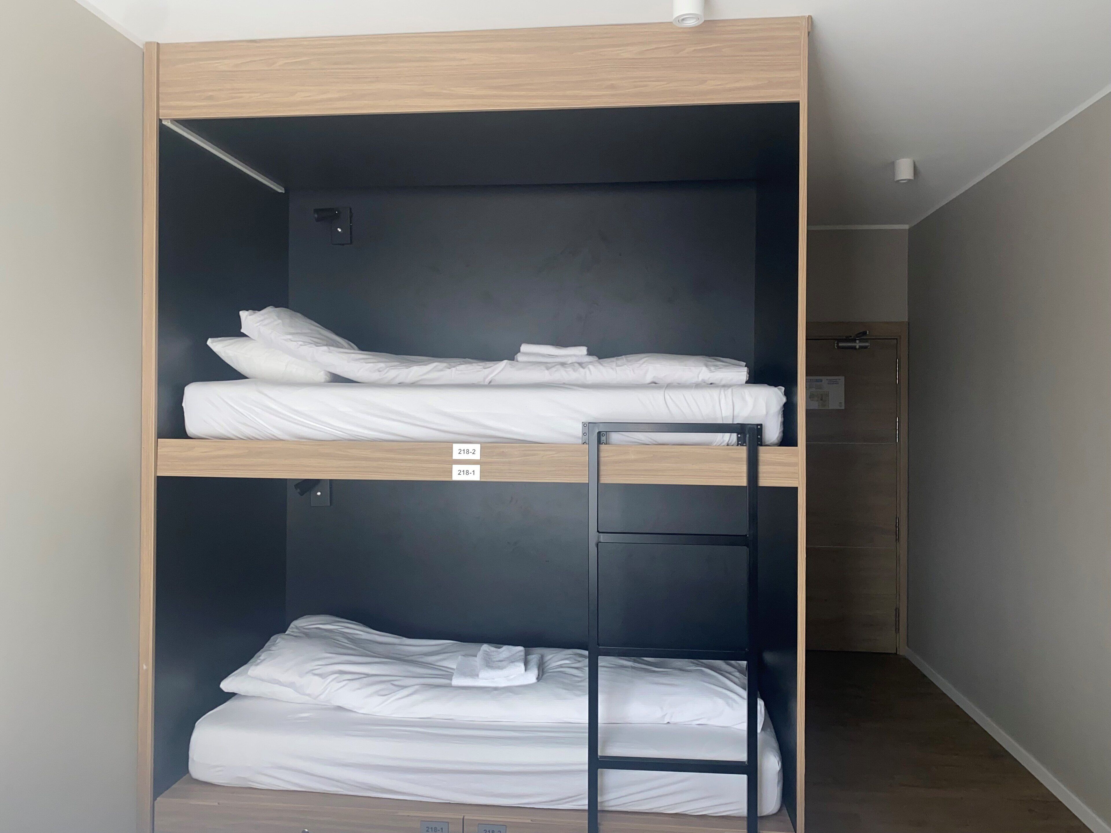 A bunk bed with two levels, each with white bedding. There is a ladder on the lower bunk.