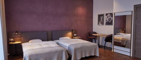 Une chambre d’hôtel avec deux lits, une petite table ronde, une chaise, un miroir et un mur orné de deux tableaux encadrés.