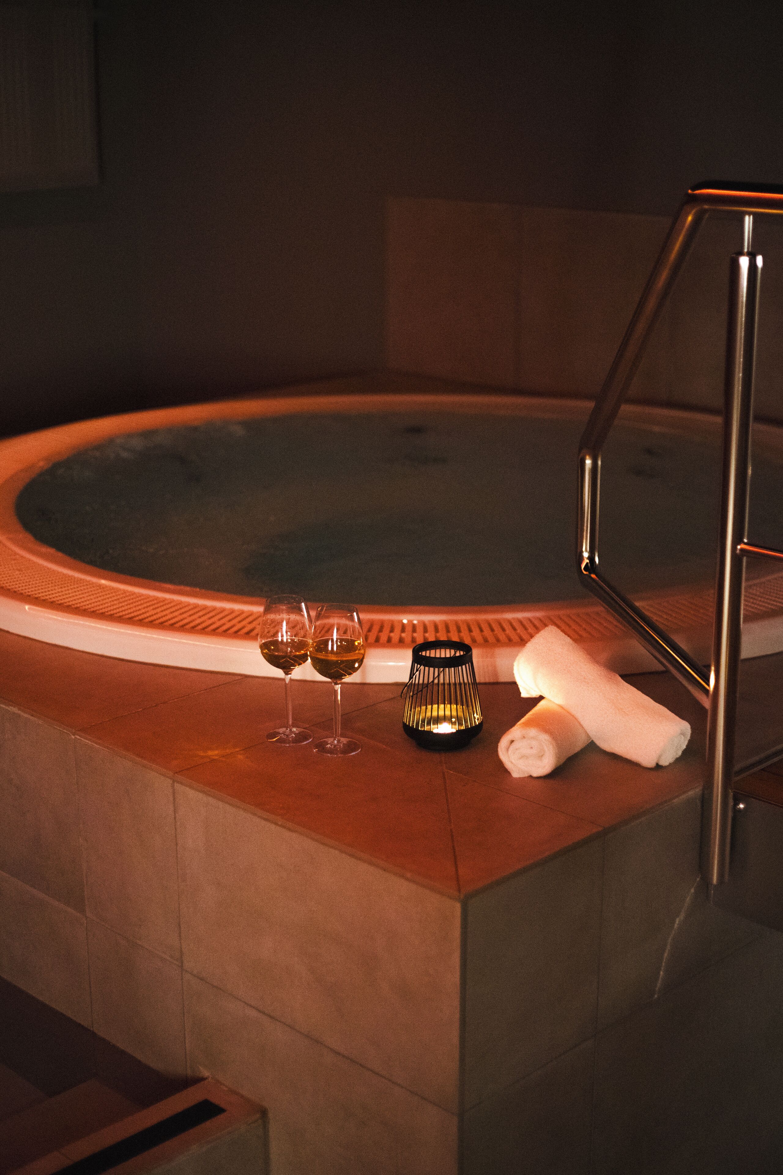 A hot tub with two glasses of wine and a candle on the edge.