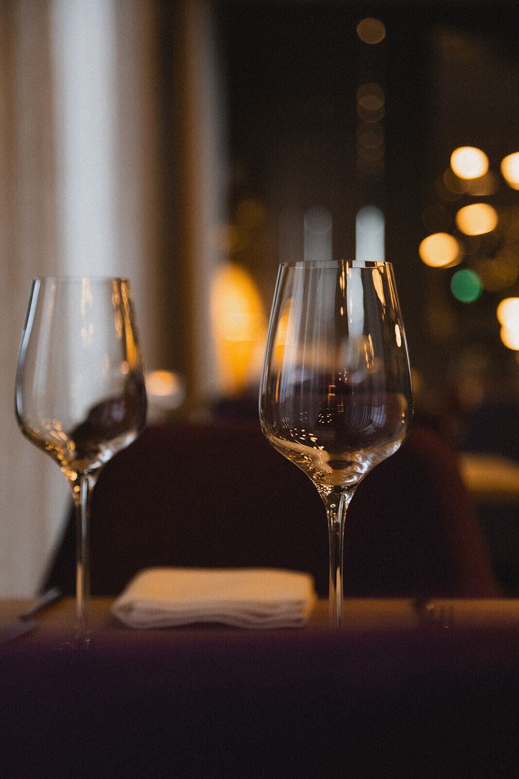 Due bicchieri da vino vuoti su un tavolo, con sfocato sfondo di luci.
