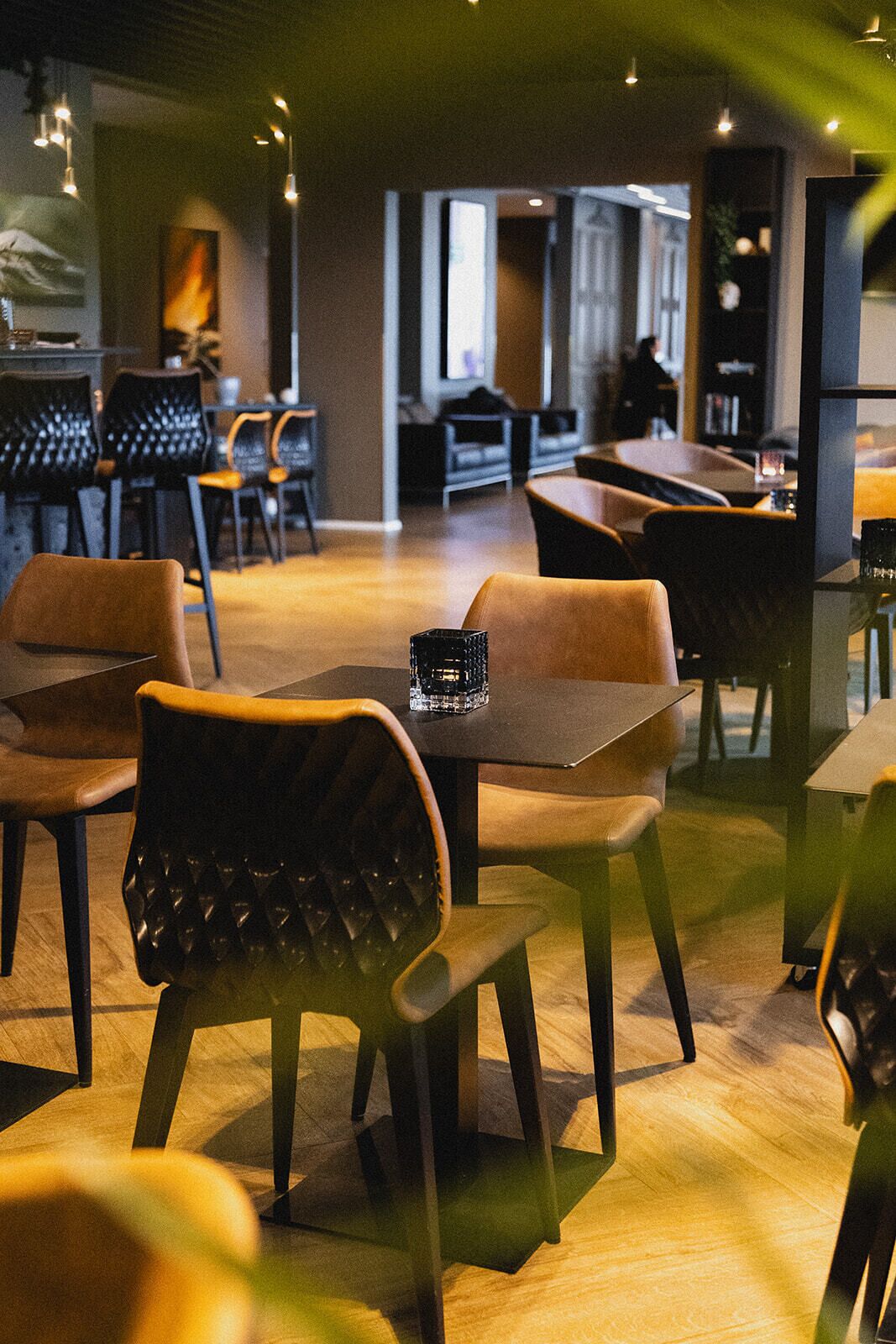 Un comedor moderno con mesas y sillas de madera, un centro de mesa de vidrio negro e iluminación cálida.
