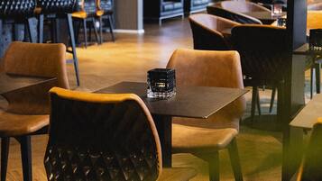 Un comedor moderno con mesas y sillas de madera, un centro de mesa de vidrio negro e iluminación cálida.