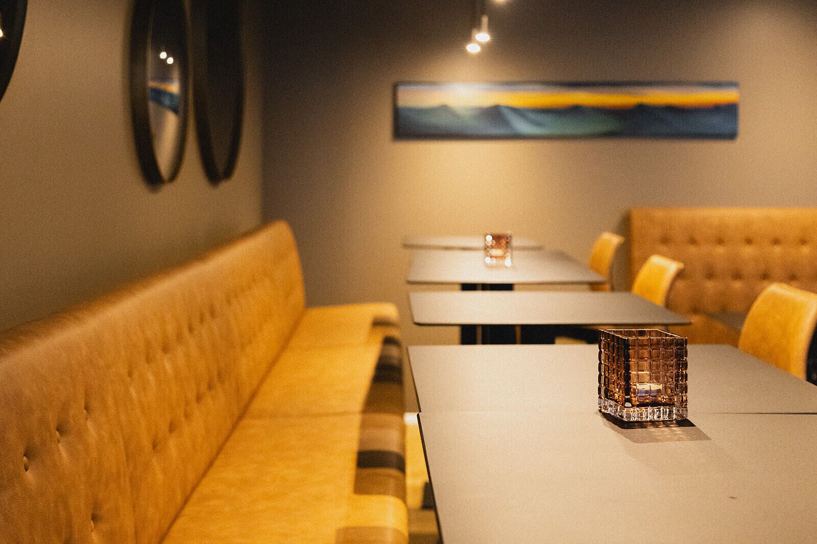 Interior de un restaurante con un banco de madera largo, una mesa con un recipiente de vidrio y un cuadro en la pared.