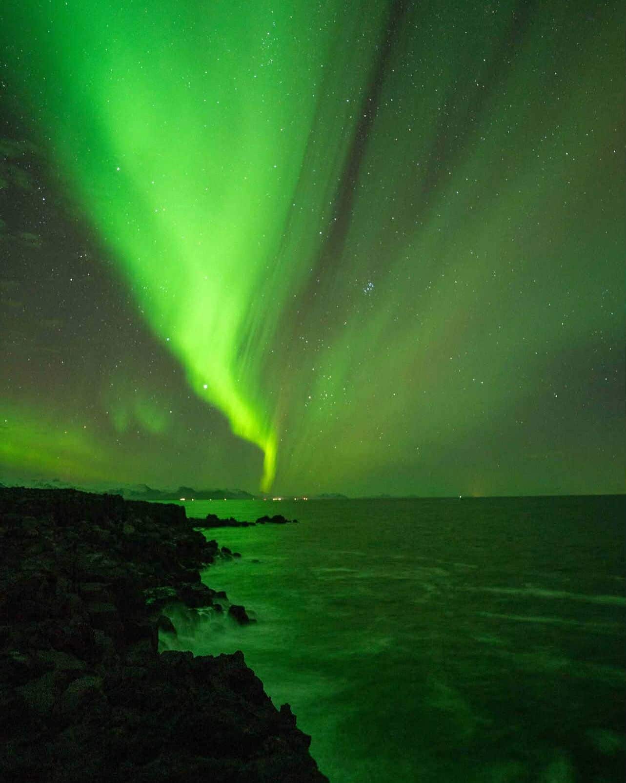 A coastal scene with a green aurora over the ocean.