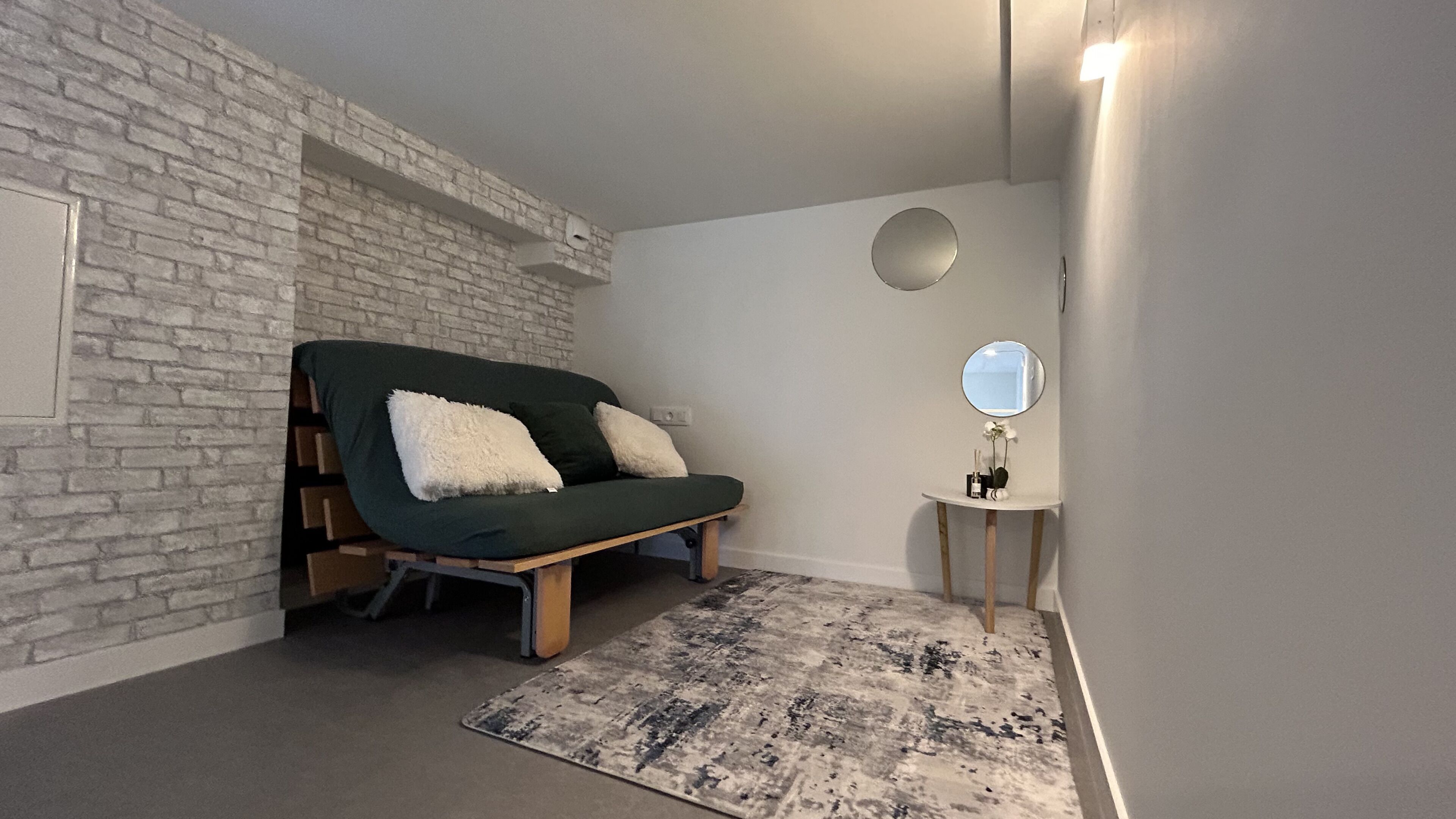 Ett litet, ombonat rum med en grön soffa, en rund spegel och en mönstrad matta.