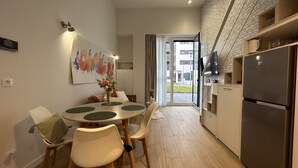 A modern kitchen with a refrigerator, a dining area with a table and chairs, and a large window with curtains.