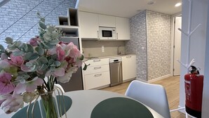 A modern kitchen with white cabinets, a microwave, and a dishwasher. There is a vase with flowers on the table.