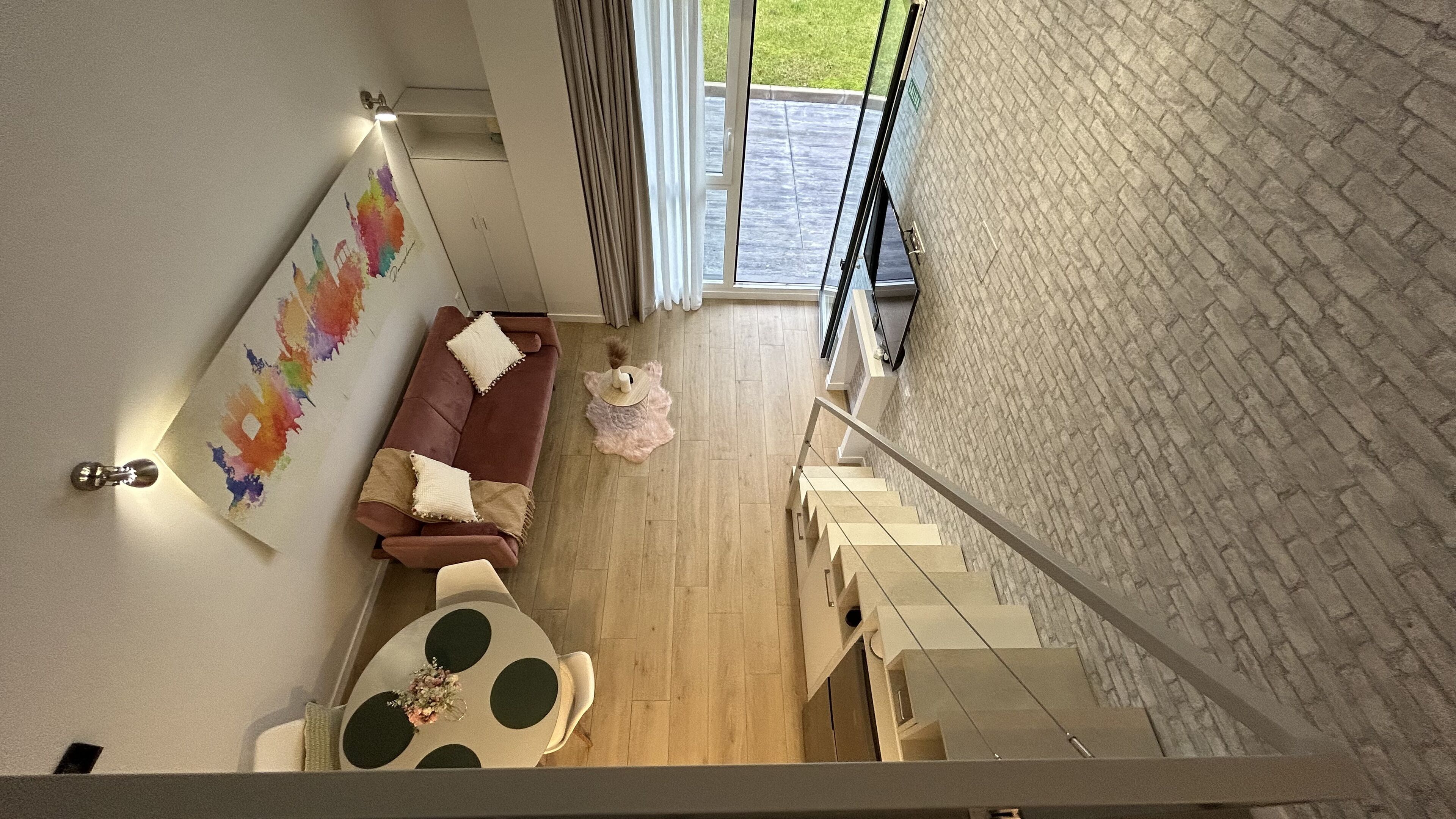 Una sala de estar moderna con un sofá marrón, una mesa redonda con un centro de mesa floral y una escalera que sube a un piso superior.