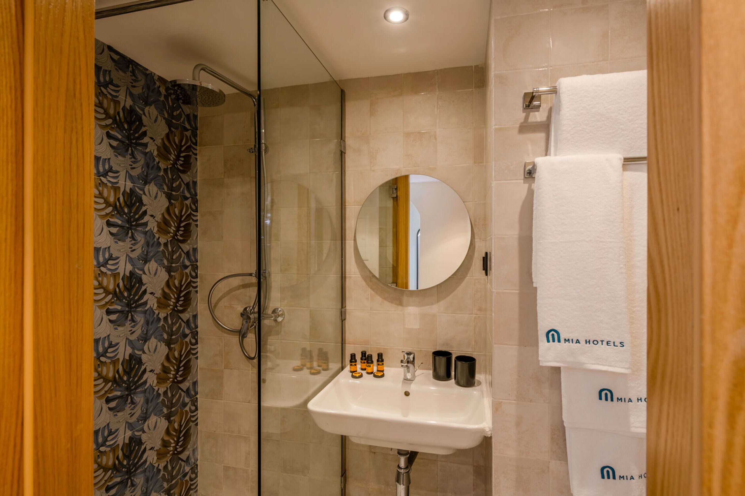 A bathroom with a glass shower enclosure, a sink with toiletries, and a mirror.