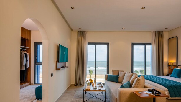 A modern hotel room with a large bed, a sofa, a coffee table, and a view of the ocean. - MIA Mazagan Bay, El Jadida (El Jadida)