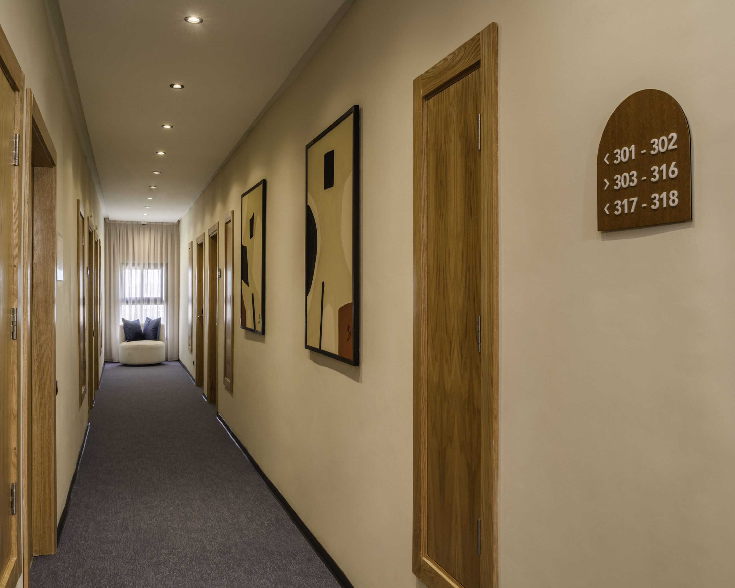 Pasillo de hotel con puertas de madera, placas numeradas y arte abstracto en las paredes.