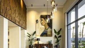 A modern living room with a sectional sofa, a large painting, and a view through large windows. - MIA Mazagan Bay, El Jadida (El Jadida)