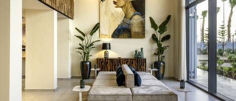 A modern living room with a sectional sofa, a large painting, and a view through large windows.