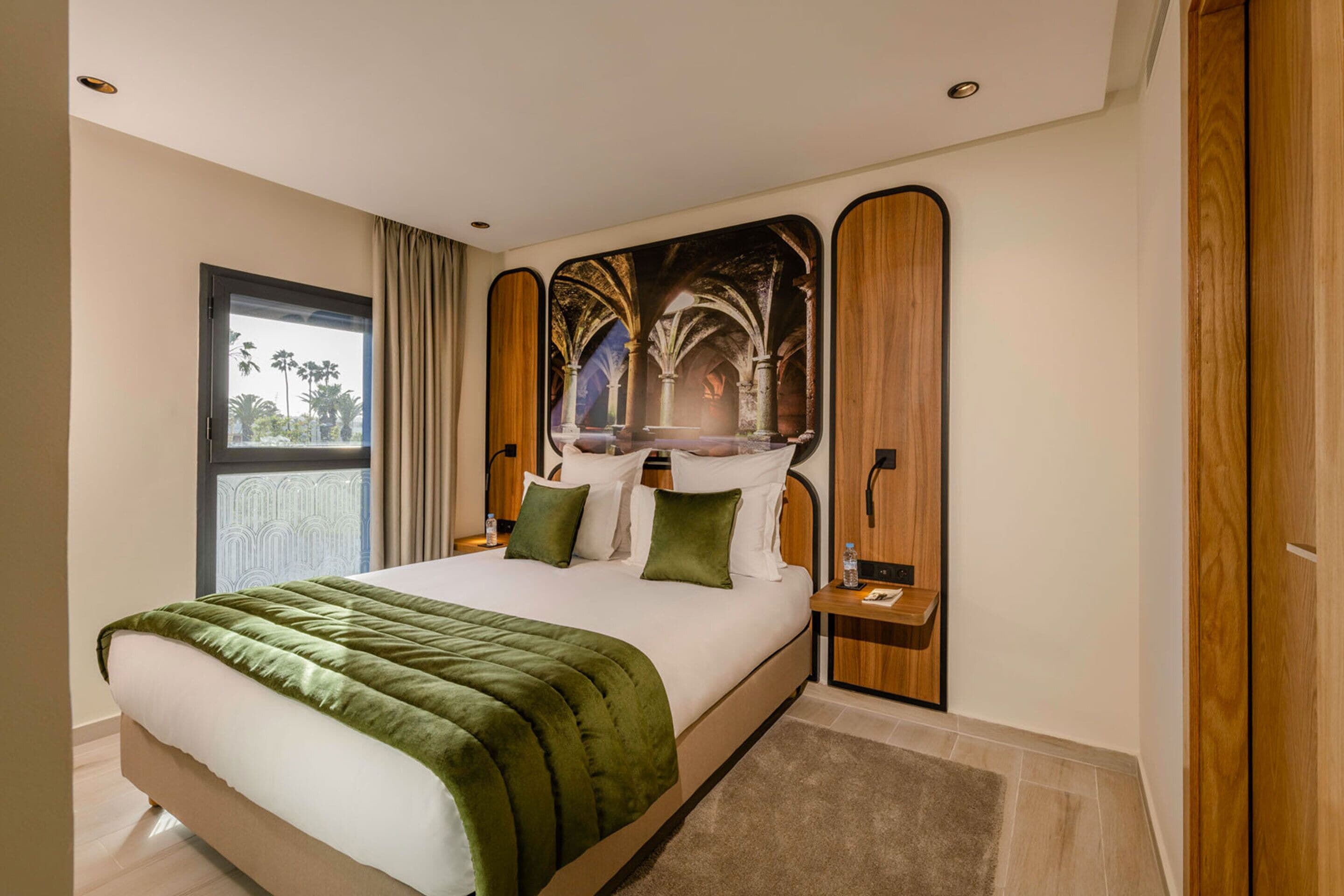A modern hotel room with a large bed, a view of palm trees, and a mural on the wall.