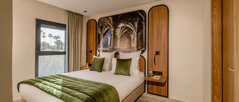 A modern hotel room with a large bed, a view of palm trees, and a mural on the wall.