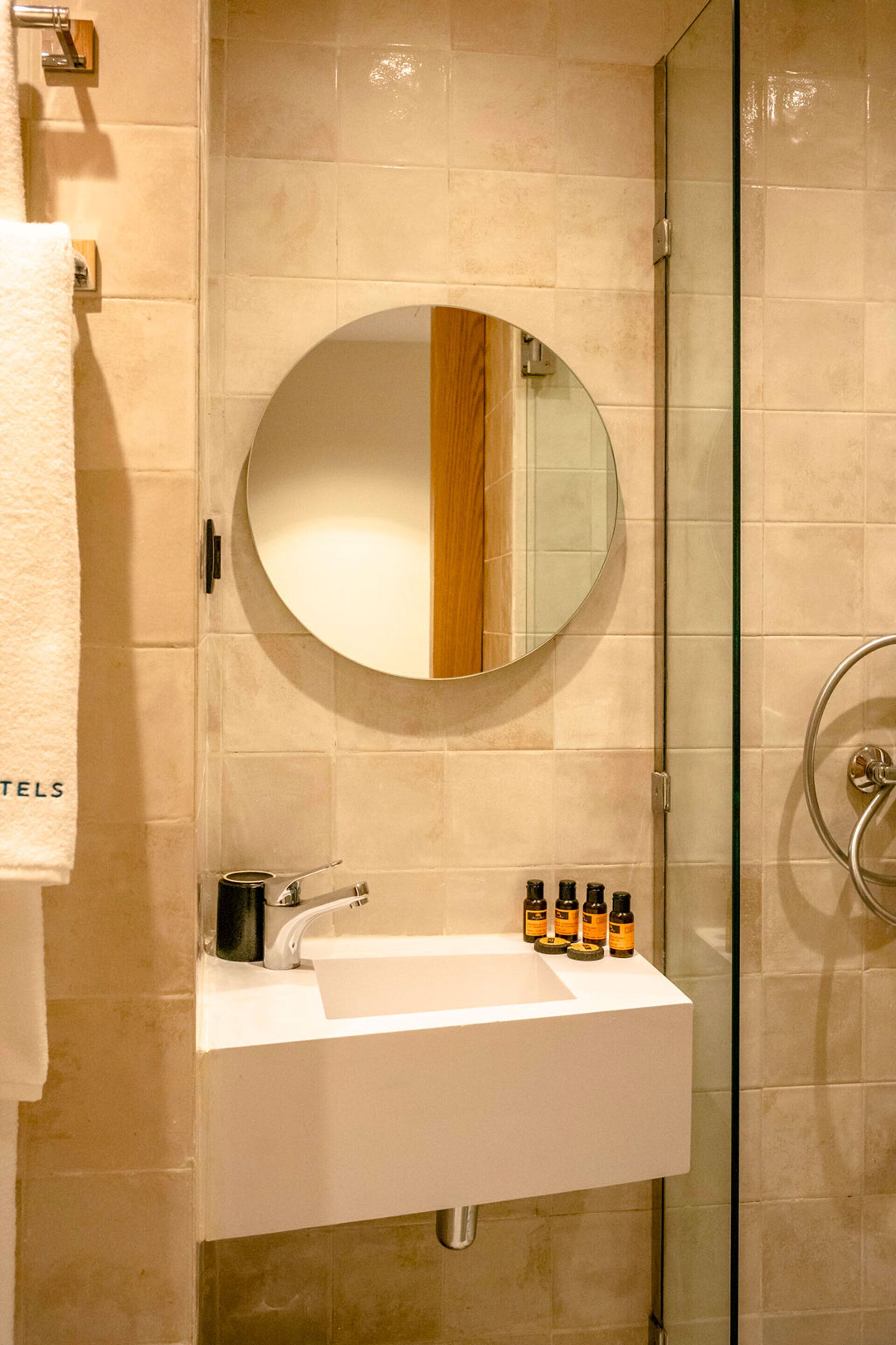 A bathroom with a round mirror, a white sink, and a glass shower enclosure.