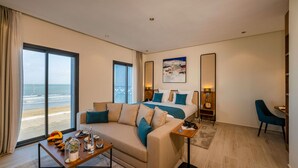 A modern hotel room with a large bed, a sofa, a coffee table, and a view of the beach. - MIA Mazagan Bay, El Jadida (El Jadida)