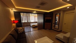 Ein modernes Wohnzimmer mit einer Couch, einem Couchtisch, einem Fernseher und einer Schiebetür, die in ein Schlafzimmer führt.