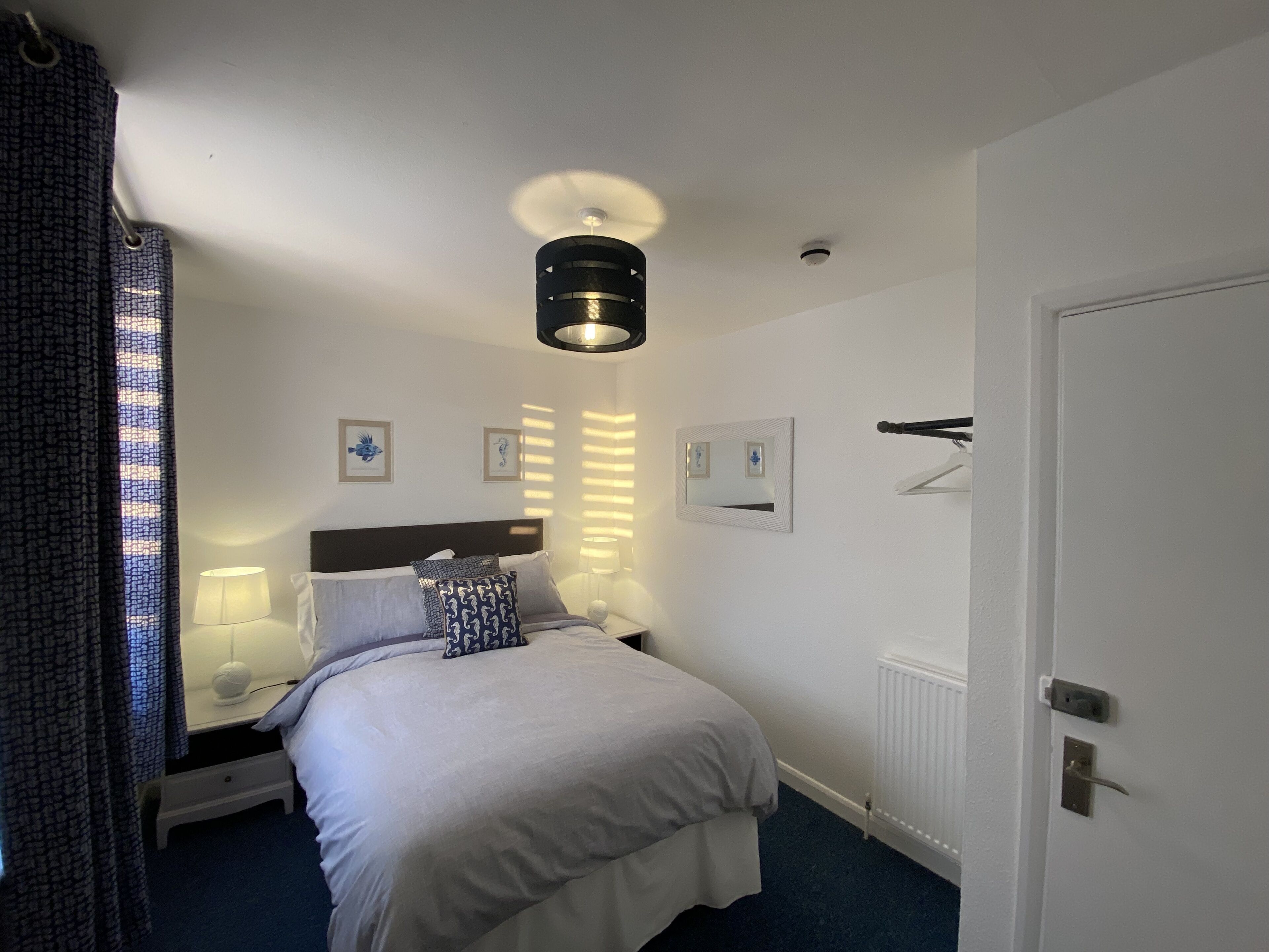 A hotel room with a bed, bedside lamps, a ceiling light, a radiator, and a door.