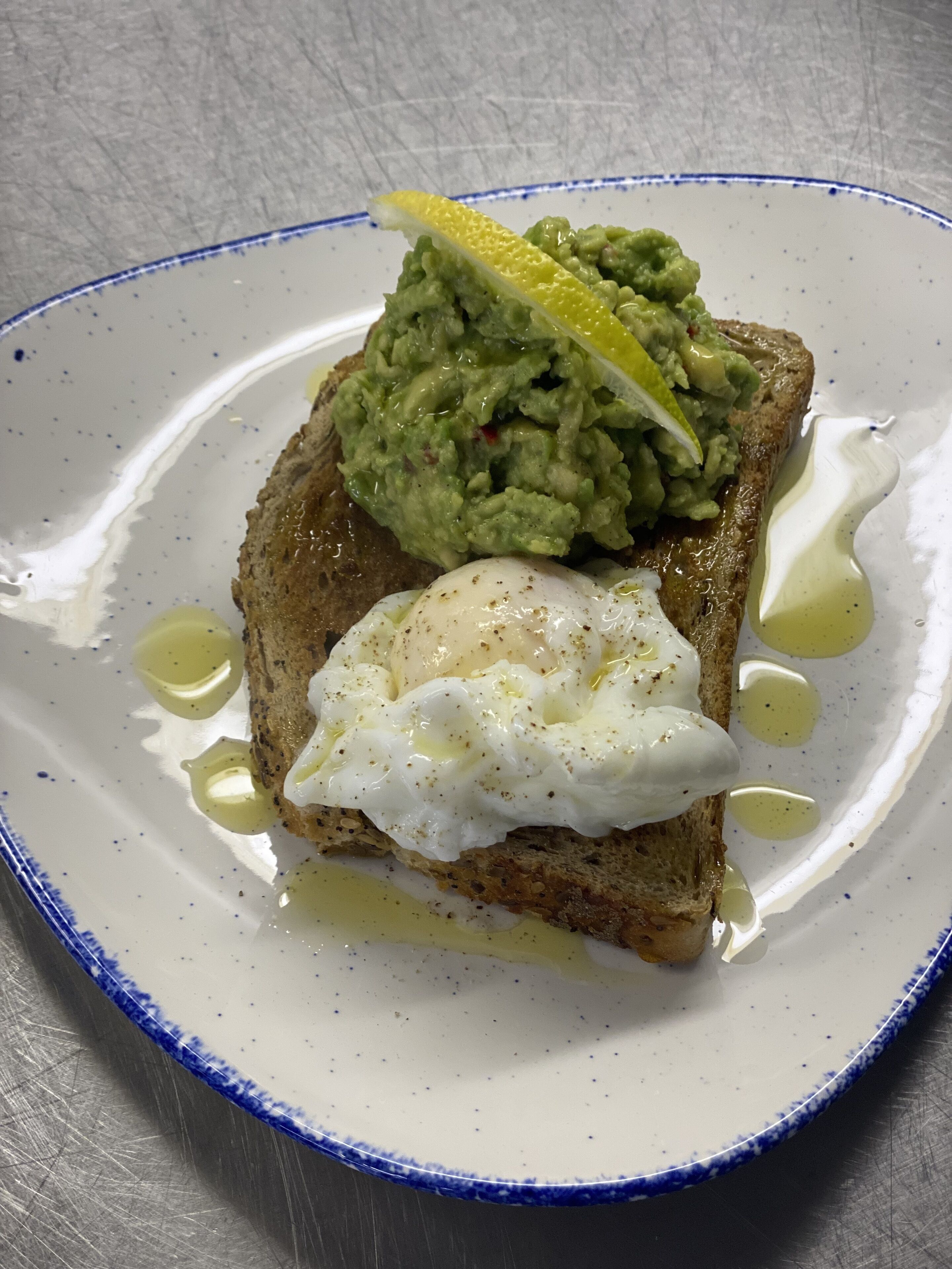 A plate with toast topped with guacamole and a poached egg, served on a white plate with blue trim.