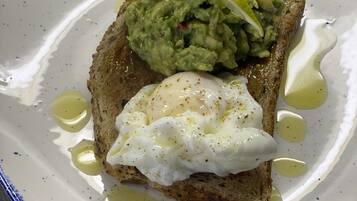 A plate with toast topped with guacamole and a poached egg, served on a white plate with blue trim.