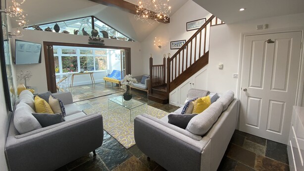 A spacious living area with a glass coffee table, two grey sofas, a wooden staircase, and a view of the outdoors. - Rooms At Babbacombe (Torquay)