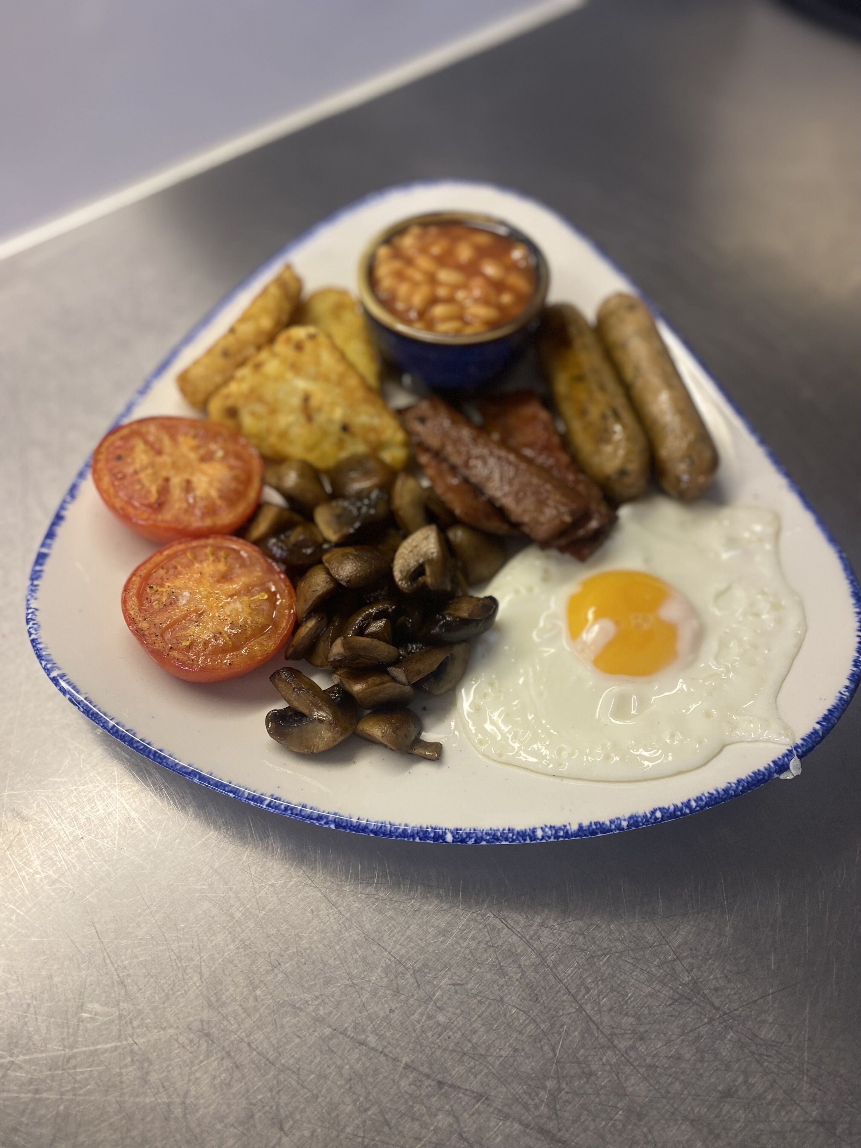 A plate of breakfast food including eggs, sausages, mushrooms, tomatoes, and beans.