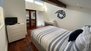 A bedroom with a bed, a TV, a desk, and a chair. There is a door leading to another room. - Rooms At Babbacombe (Torquay)