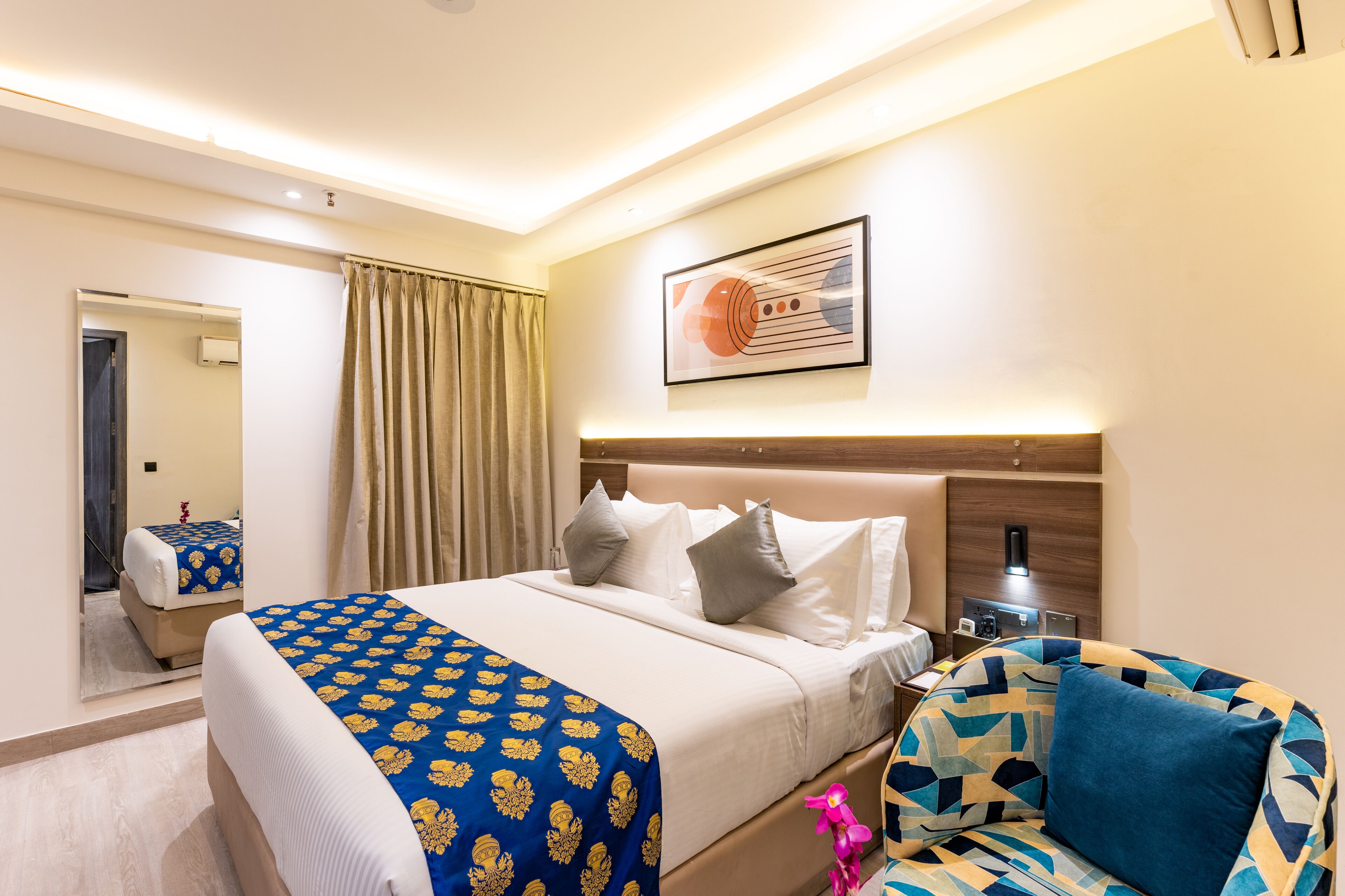 Una habitación de hotel con cama, una silla, un espejo y una obra de arte colgada en la pared.