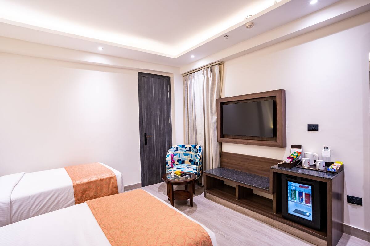 A hotel room with two beds, a TV, a small table with a coffee maker, and a mini-fridge.