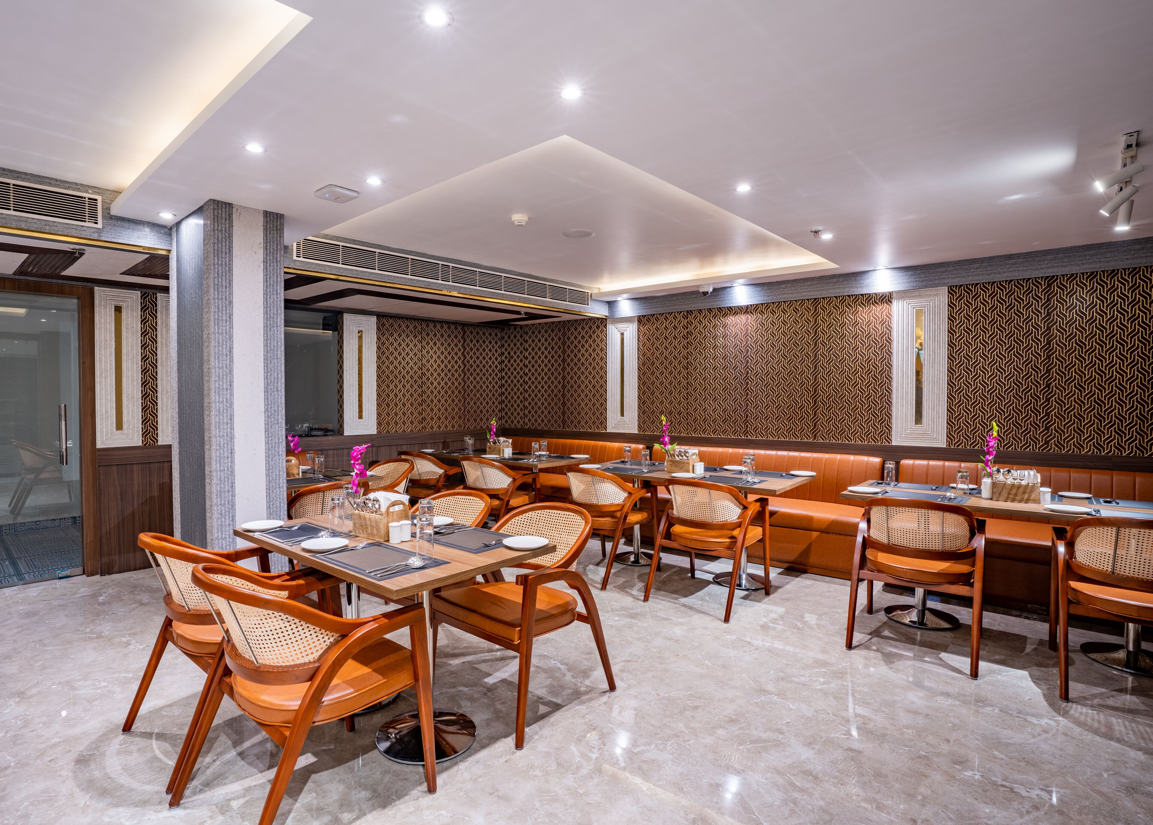 Un restaurant avec des banquettes et des tables, des chaises en bois et un mur orné de motifs.