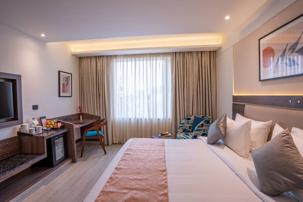 A hotel room with a bed, a desk, a television, and a window with curtains.