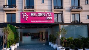 L’entrée d’un hôtel, avec une enseigne bien visible indiquant « RE:GEN:TA INN by Royal Orchid Hotels Ltd. ». Des plantes en pot sont disposées devant l’entrée.