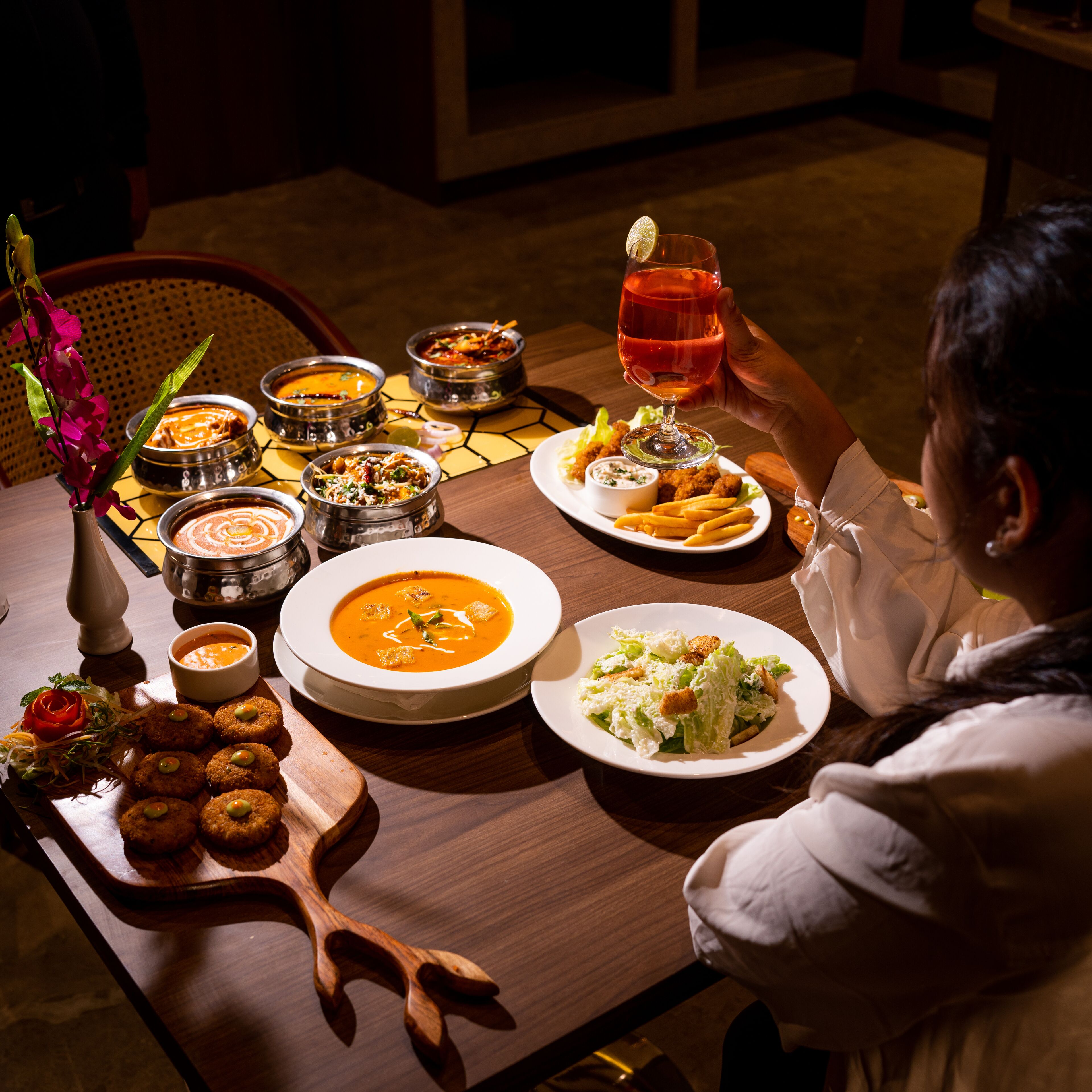 A dining table with various dishes, including soup, salad, and bread, and a person holding a glass of red wine.