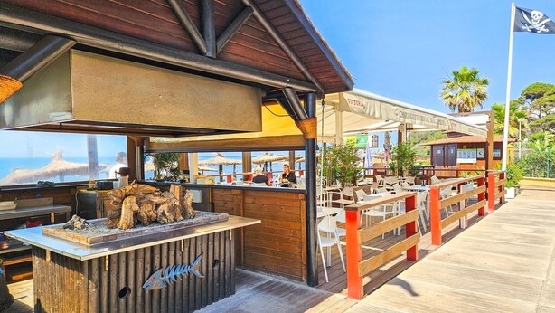 Un restaurante frente al mar con terraza, barra de madera y vistas al océano.
