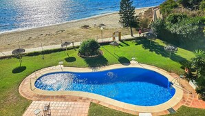 Una piscina con vista al mar, rodeada de un jardín y una terraza pavimentada.
