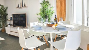 Un comedor con una mesa redonda dispuesta para cuatro, sillas blancas, una planta en maceta y una gran tabla de surf de madera en la pared.
