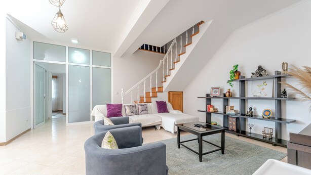 En moderne stue med trappe, sofa, sofabord og bogreol.