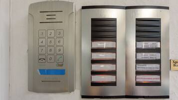 Ascensor empotrado en la pared con teclado numérico y panel de botones etiquetados para diferentes apartamentos.