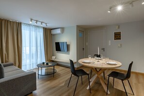 A modern living room with a sofa, a round dining table set for four, and a TV mounted on the wall. - Leviosa apartment airport by Airstay (Spata-Artemida)