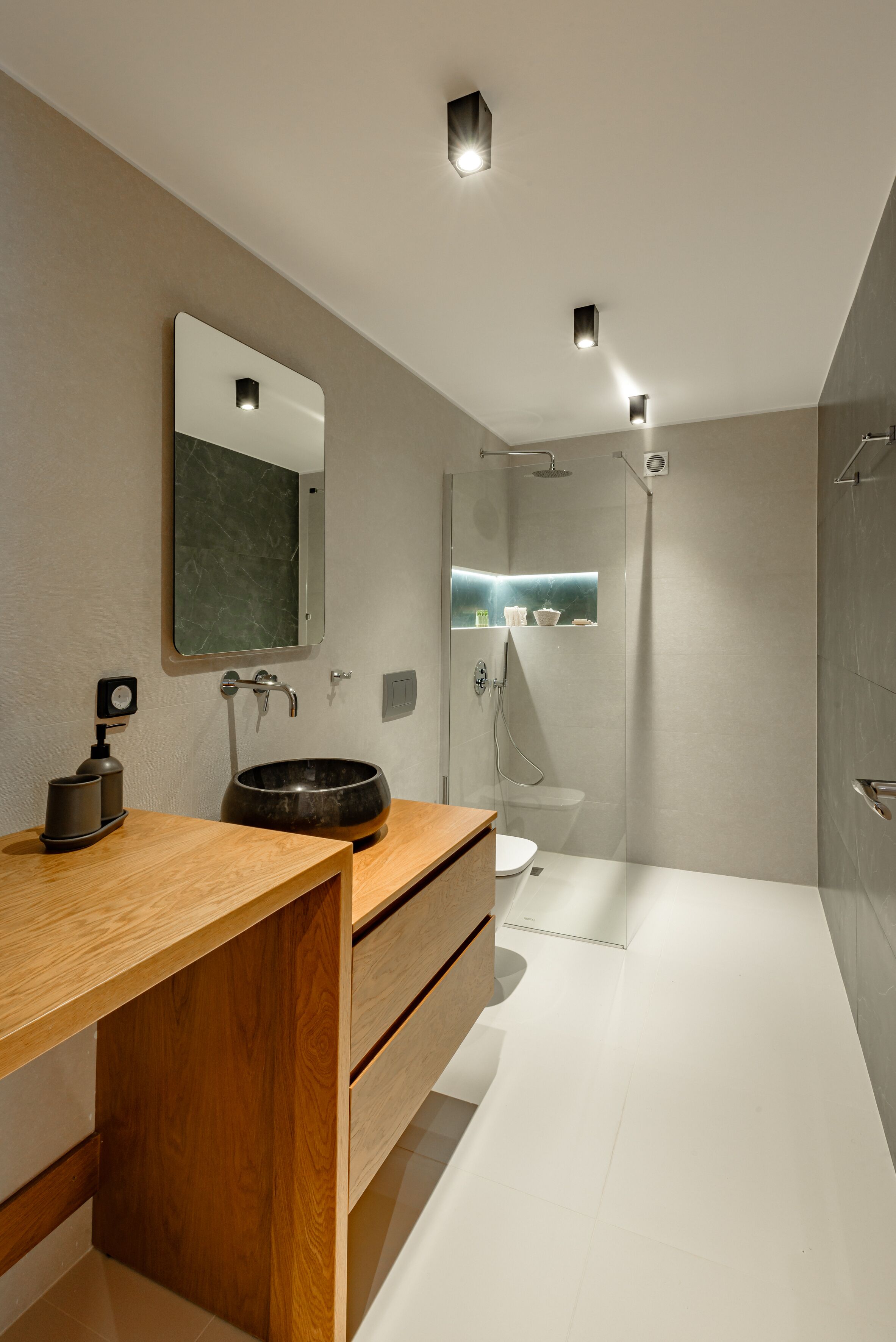 A modern bathroom with a wooden vanity, a round sink, a mirror, and a shower area.