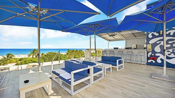 Una terraza en la azotea con sombrillas azules, muebles blancos y vistas a la playa.