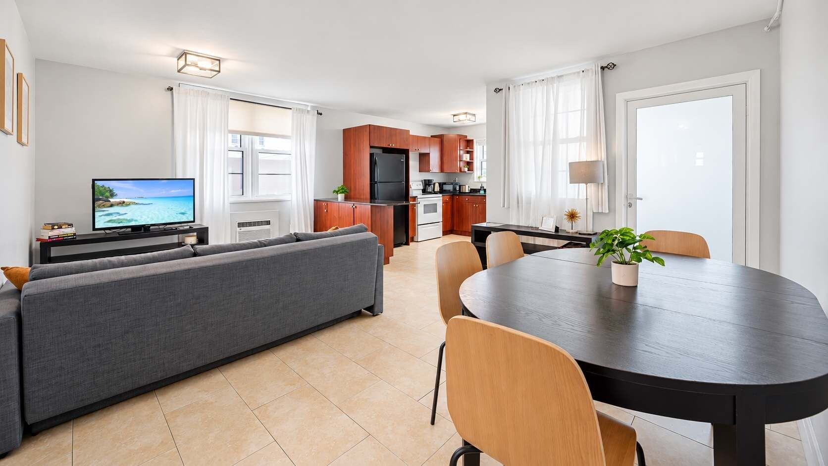Un salon moderne comprenant un canapé, une table à manger avec des chaises, un coin cuisine avec des meubles en bois et un téléviseur posé sur un meuble.