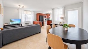 Una sala moderna con un sofá, una mesa de comedor con sillas, una zona de cocina con armarios de madera y un televisor sobre un mueble.