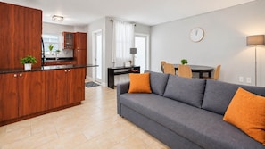 Una sala de estar moderna con un sofá gris, armarios de madera y una zona de comedor con una mesa y sillas.
