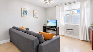Un salon moderne avec un canapé gris, un téléviseur à écran plat et une fenêtre avec des rideaux.
